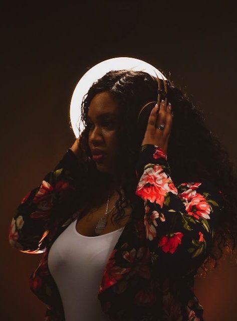 Lori Barr in a floral jacket, hands raised to her hair, lit by a ring light